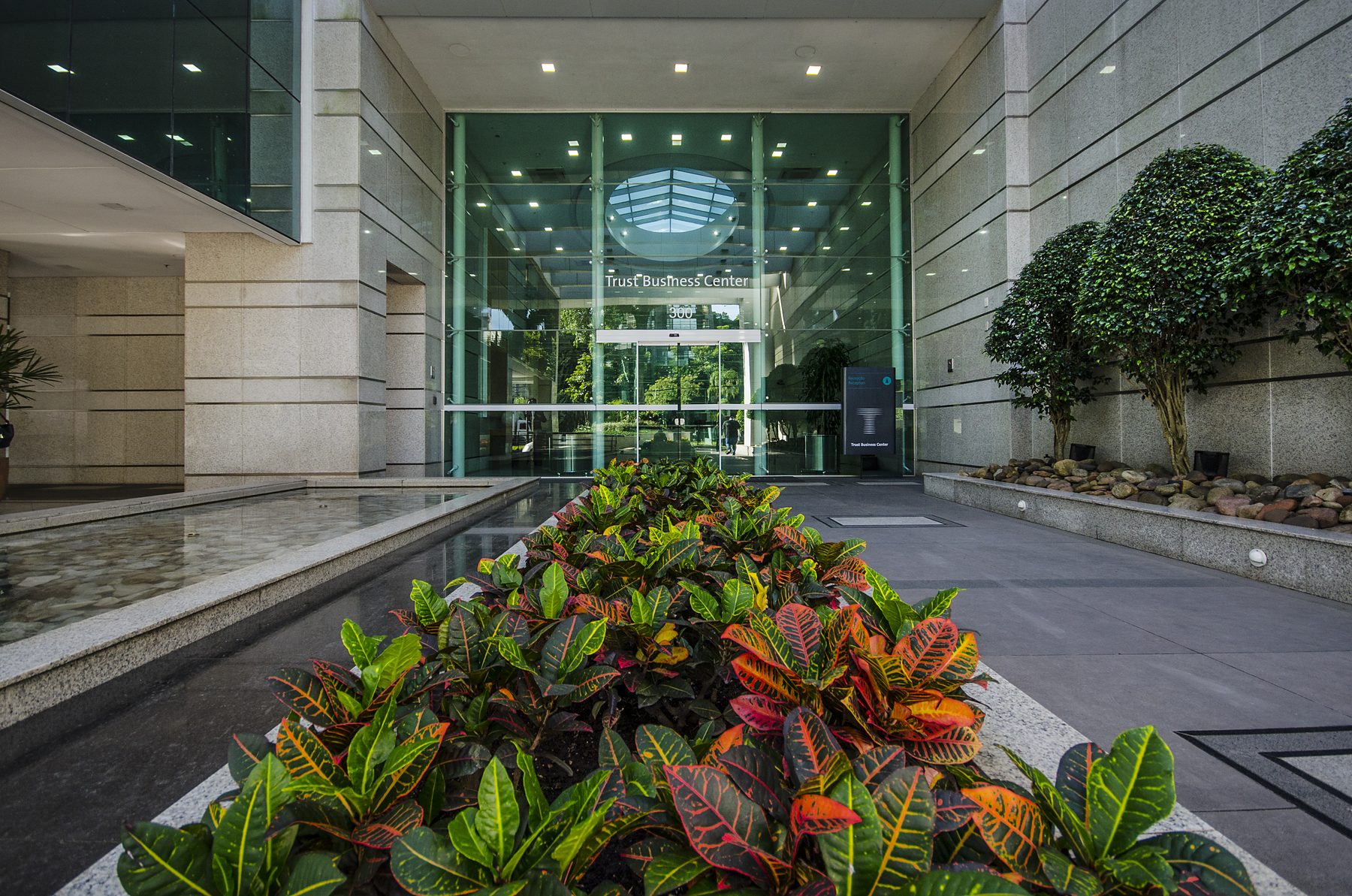 Acesso principal do Trust Business Center, com espelho d'água e jardim.